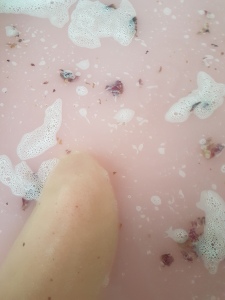 A woman's leg bathes in a pink bath with rose petals. Photo by Jennifer Ratcliffe