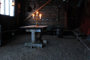 An Empty old barn with a candelabra centred on a wooden table. The candles are lit as is a swinging lantern near the window. Photo by Jennifer Ratcliffe Boygoynes, Norway 2013